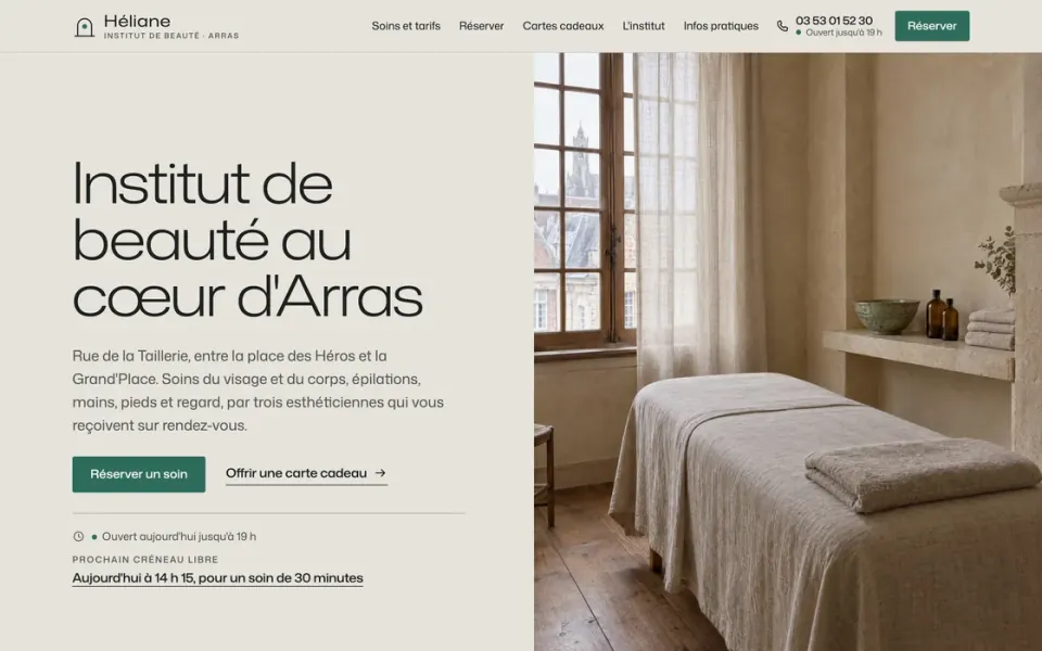 Site de démonstration de l'institut de beauté fictif Héliane à Arras : cabine de soin baignée de lumière, lit couvert de lin devant une fenêtre sur les toits, titre « Institut de beauté au cœur d'Arras » et bouton Réserver un soin